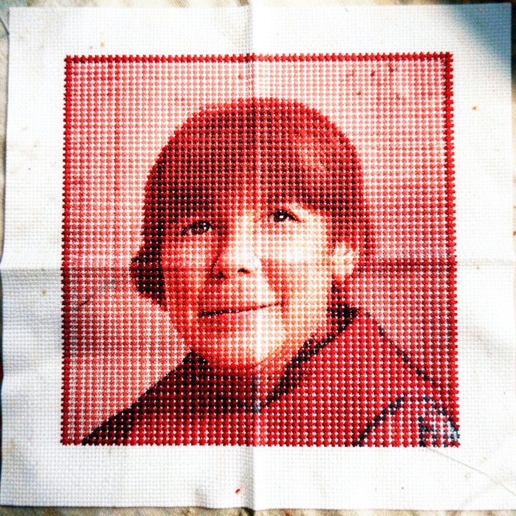 A close-up documentary photograph of a needlepoint sampler cloth showing dozens of cross-stitch variations in muted earth tones against natural linen.